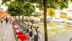 Række af cykler parkeret langs fortov med borde og stole i nærheden.