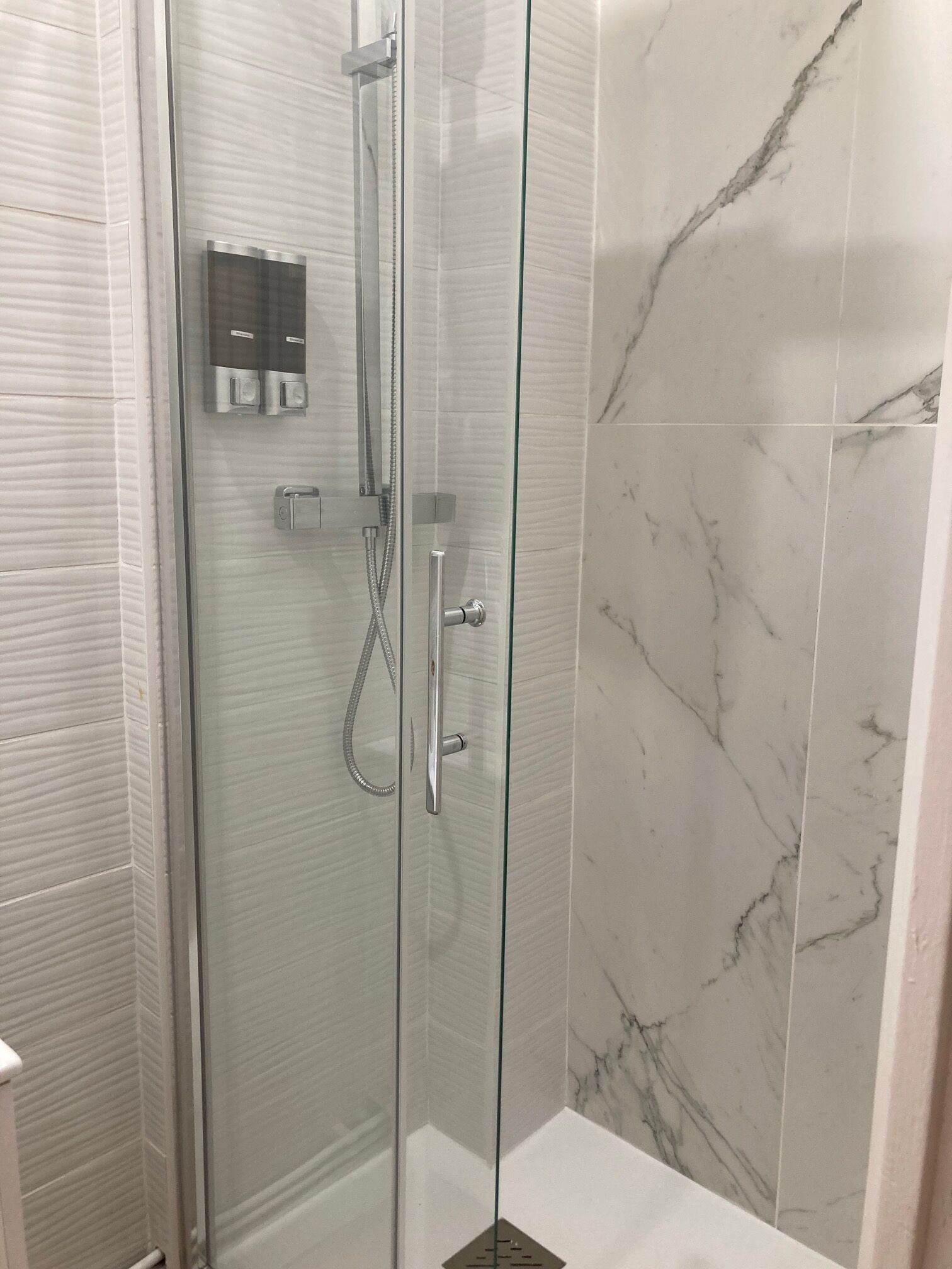 A glass-enclosed shower with a handheld showerhead and a wall-mounted control panel.