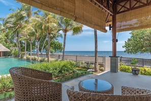A poolside area with wicker furniture, a glass table, and a view of the ocean. - In Balance Resort (Banjar)