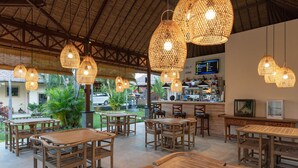 An outdoor seating area with wooden tables and chairs, surrounded by lush greenery and a thatched roof structure. - In Balance Resort (Banjar)