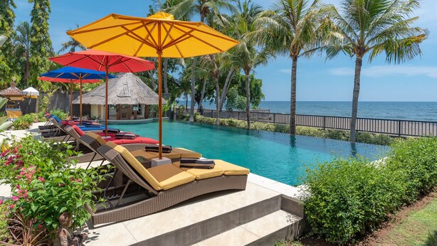A poolside area with lounge chairs and umbrellas, a thatched-roof structure, and a view of the ocean. - In Balance Resort (Banjar)