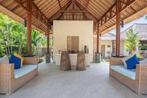 A covered outdoor seating area with wicker furniture and a central counter. - In Balance Resort (Banjar)