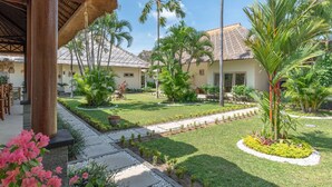 A resort with a thatched-roof structure, palm trees, and a well-maintained garden. - In Balance Resort (Banjar)