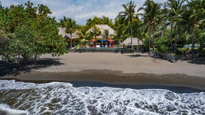 A beachside resort with a sandy beach, palm trees, and a building with colorful umbrellas. - In Balance Resort (Banjar)