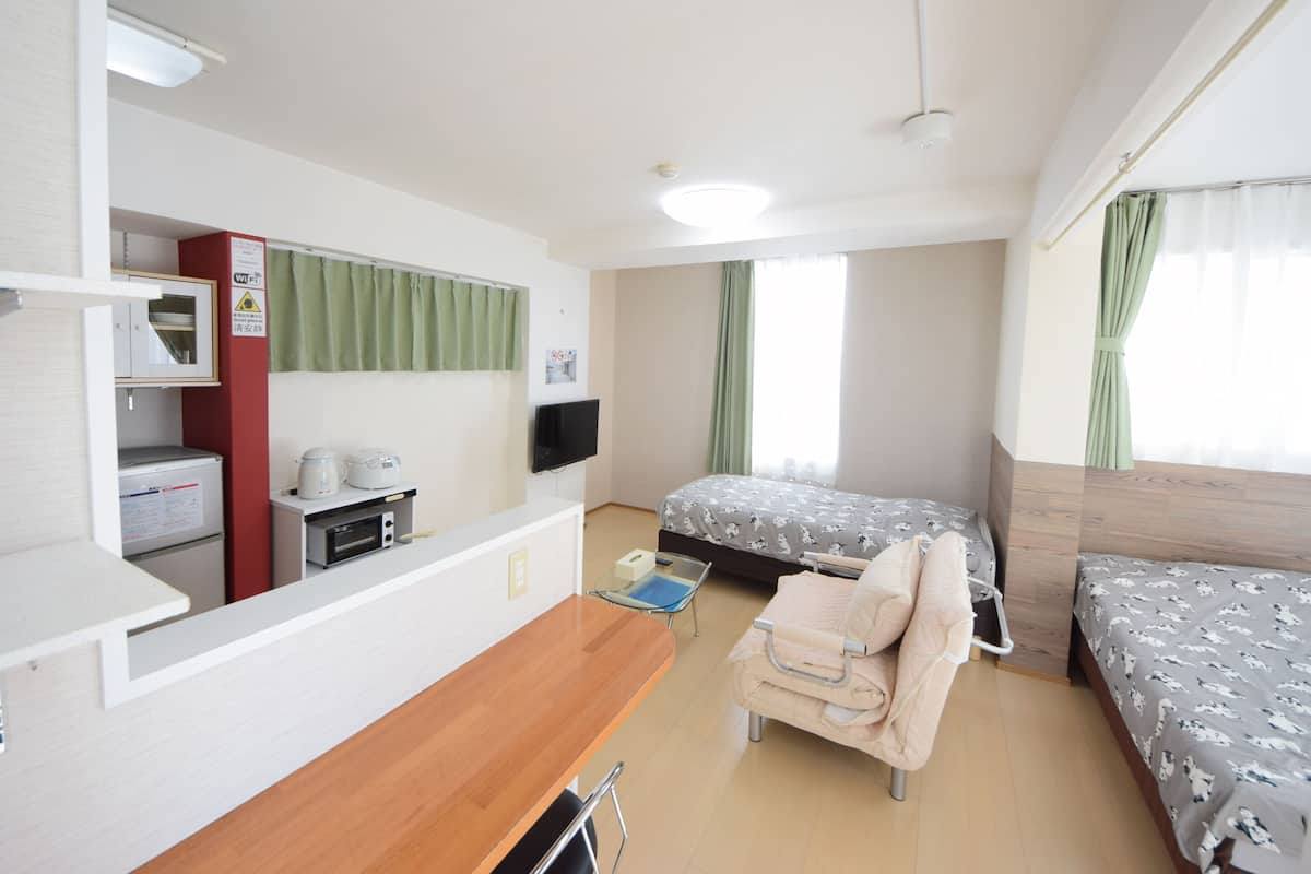 A room with a kitchenette, two beds, a sofa, and a TV.