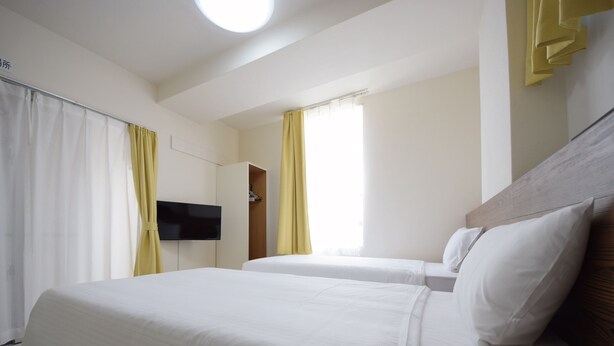 Une chambre d’hôtel avec deux lits, une télévision, une armoire et une fenêtre avec des rideaux.