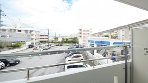 Une vue depuis un balcon donnant sur une rue bordée de voitures garées et d’immeubles.