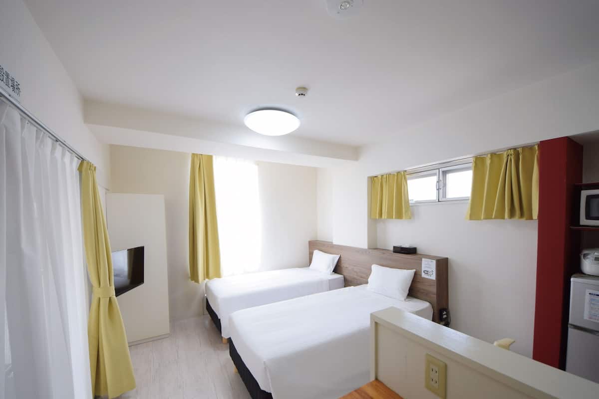 A hotel room with two beds, a TV, a microwave, and a small kitchenette.
