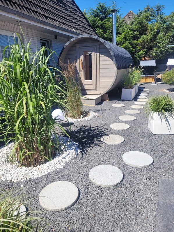 A spa-like structure with a curved roof, surrounded by gravel and stepping stones, and adjacent to a building with a tiled roof.