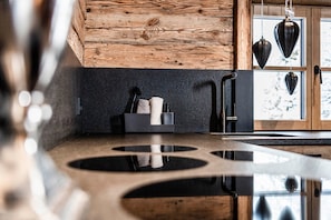 A kitchen with a wooden ceiling, a black countertop, and hanging kitchen utensils.