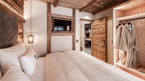 A bedroom with a wooden ceiling, a bed with white bedding, a hanging light fixture, and a wooden wardrobe with robes.