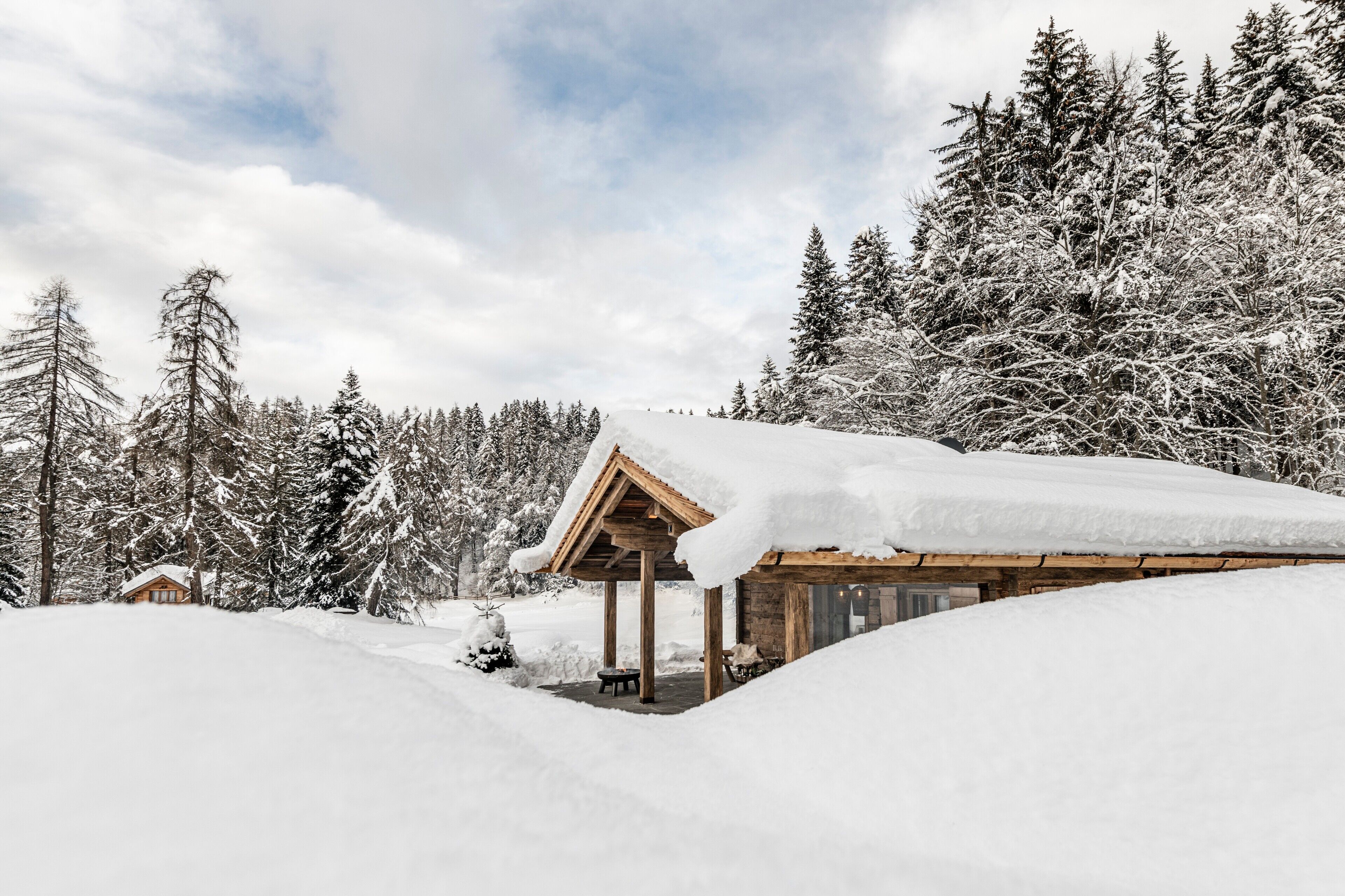Una baita di legno con tetto innevato, circondata da alberi carichi di neve e un cielo sereno.