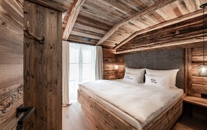 A wooden cabin-style bedroom with a bed, pillows, and a window with curtains.