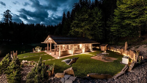 A cabin with a patio, surrounded by a forest.