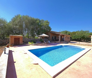 Une piscine avec une terrasse carrelée, un petit jardin agrémenté d’un kiosque et un mur en pierre.