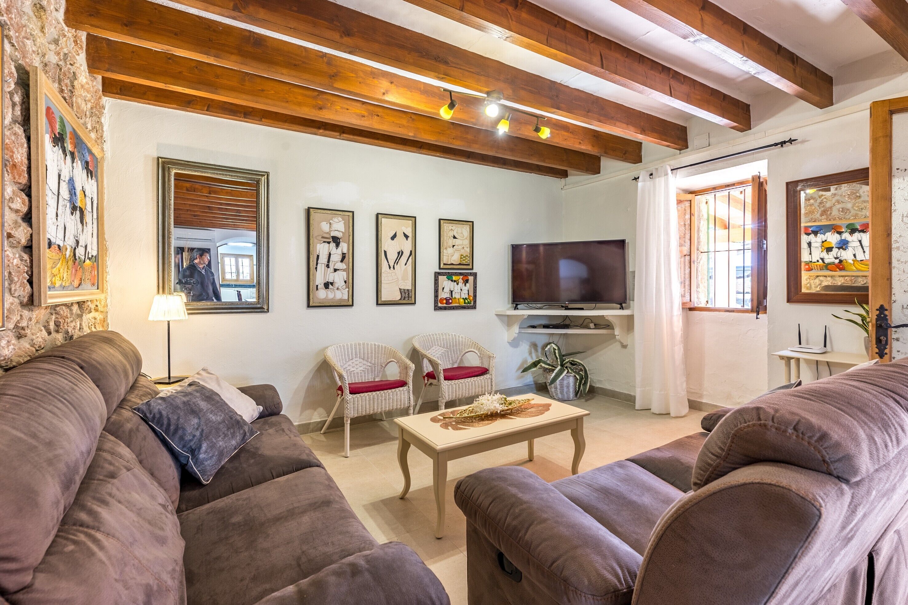 A living room with a brown sofa, two wicker chairs, a wooden coffee table, a TV, and artwork on the walls.