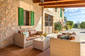 A stone-walled room with wicker furniture, a glass coffee table, and a view of the street. - Finca Can Pou Petit with Mountain View, Pool, Wi-Fi, A/C, Terrace & Garden (Pollensa)