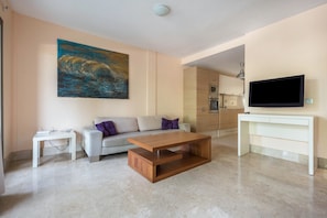 A modern living room with a sofa, coffee table, flat-screen TV, and a painting on the wall.