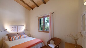 Een slaapkamer met een bed, een raam, een stoel en een tafel met een vaas.