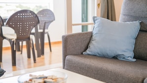 A living room with a grey sofa, a blue pillow, a glass bowl with snacks, and a dining area with black chairs. - Apartment "White Sands 306" on the Beach with Sea View, Pool (Arenal d'en Castell)