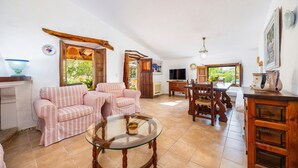 A spacious living area with a sofa set, a glass coffee table, and a dining table with chairs. - Villa 'Can Tonet' with Mountain View, Wi-Fi and Air Conditioning (Port de Pollença)