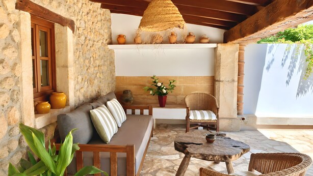 A stone-walled room with a wooden bench, a wicker chair, a round table, and a hanging light fixture. - Villa 'Can Tonet' with Mountain View, Wi-Fi and Air Conditioning (Port de Pollença)