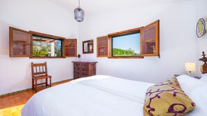 A bedroom with a bed, wooden furniture, a dresser, and windows with open shutters. - Villa 'Can Tonet' with Mountain View, Wi-Fi and Air Conditioning (Port de Pollença)
