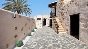 A narrow stone pathway leading to a building with a stone facade and a palm tree in the background. - "Casa Rural Andresito" with Mountain Views, Pool, Wi-Fi, and Terrace (Pájara)