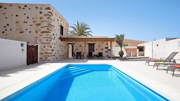 A swimming pool with lounge chairs, a stone building, and a clear sky. - "Casa Rural Andresito" with Mountain Views, Pool, Wi-Fi, and Terrace (Pájara)