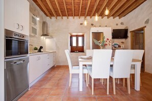 Een moderne keuken met witte kasten, een inbouwoven en een eethoek met witte stoelen en een houten tafel.