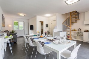 A modern kitchen with a wooden staircase, white dining area, and a flat-screen TV.