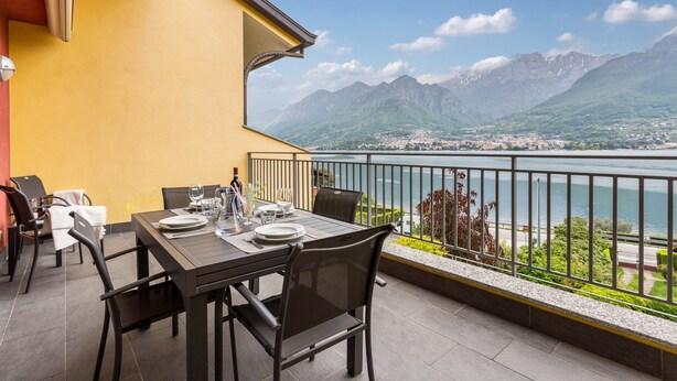 A terrace with a table set for dining, overlooking a lake and mountains.
