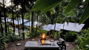 A circular outdoor seating area with a fire pit, surrounded by tropical plants and a stone pathway. - 2 x queen bedrooms, 2 x ensuite's, 1 guest lounge, outdoor bbq kitchen and pool. (Currumbin Valley)