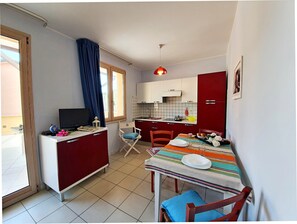 Kompakti keittiö, jossa on ruokailutila, televisio ja ikkuna, jossa on verhot.