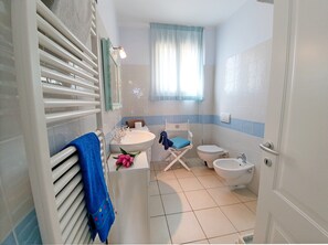 A bathroom with a white sink, toilet, bidet, and a shower area.