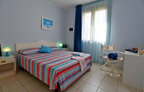 A bedroom with a bed, a desk, a chair, a lamp, and a window with curtains.