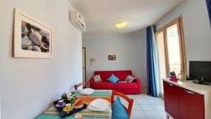 Un coin repas avec une table dressée pour deux personnes, un canapé rouge, un téléviseur et un espace cuisine.