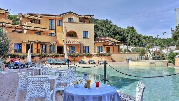 Un espace aménagé au bord de la piscine avec des chaises longues et une table, un bâtiment doté de balcons et une vue dégagée sur la piscine.