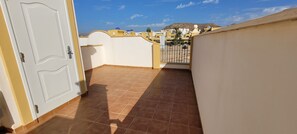 A balcony with a tiled floor, a white door, and a view of a yellow building with blue domes in the background.