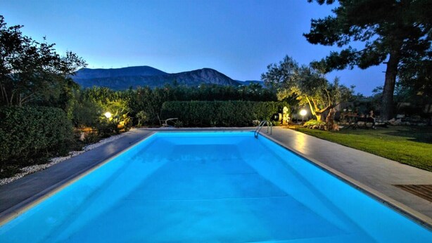 Una piscina rectangular con superficie de agua azul cristalina, rodeada por una solana pavimentada e iluminada por luces ambientales.