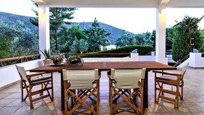 Una mesa de madera con cuatro sillas en un entorno exterior con vistas a árboles y colinas.