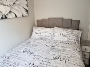 Quarto com cama, almofadas e mesa de cabeceira.