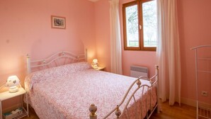A bedroom with a bed, a nightstand, a window with curtains, and a radiator.