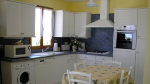 A compact kitchen with white cabinets, a washing machine, a microwave, and a dining table with chairs.