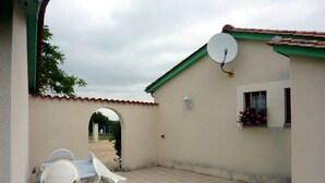 A patio with white plastic chairs and a table, a satellite dish, and a small window with flowers.