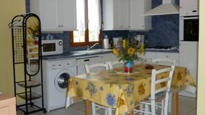 A compact kitchen with white cabinets, a washing machine, a microwave, and a dining table with a yellow floral tablecloth.