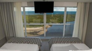 A hotel room with two beds, a TV, and a large window offering a view of a beach and ocean. - Tryp Pernambuco (Jaboatao dos Guararapes)