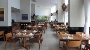 A spacious restaurant with multiple dining tables and chairs, large windows, and a modern interior design. - Tryp Pernambuco (Jaboatao dos Guararapes)
