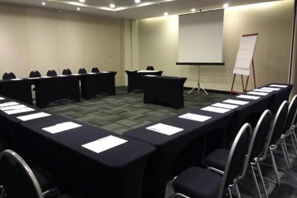 A conference room with a long table, chairs, a projector screen, and a flip chart.