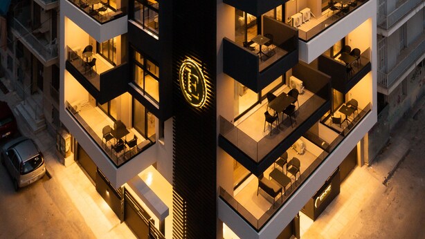 A multi-story hotel with balconies, outdoor seating, and a prominent logo on the facade. - LUX&EASY Athens Downtown Apartments (Athens)